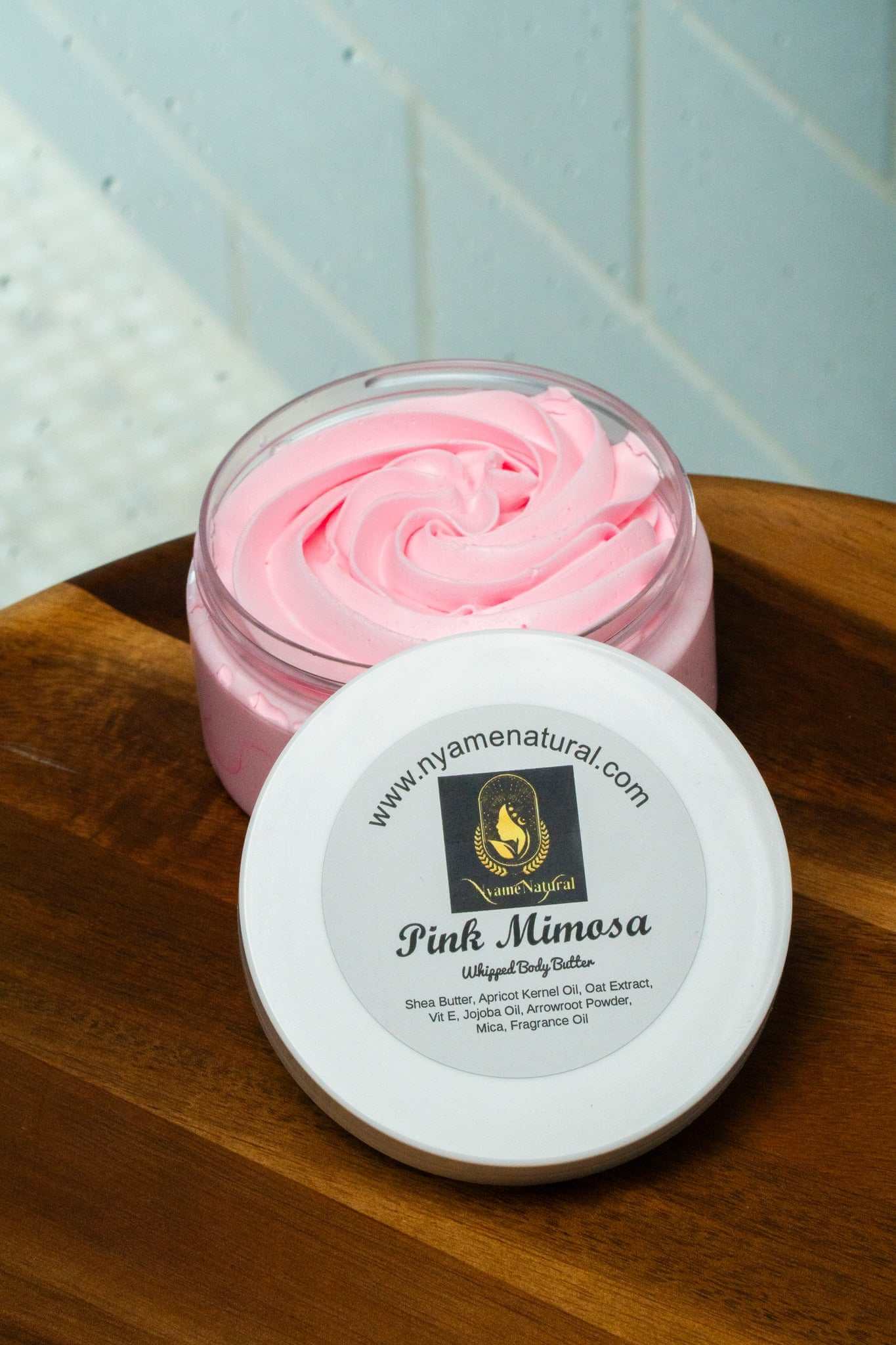 Pink Mimosa Body Butter in a clear jar, featuring a silky-soft pink texture and a printed label on top.