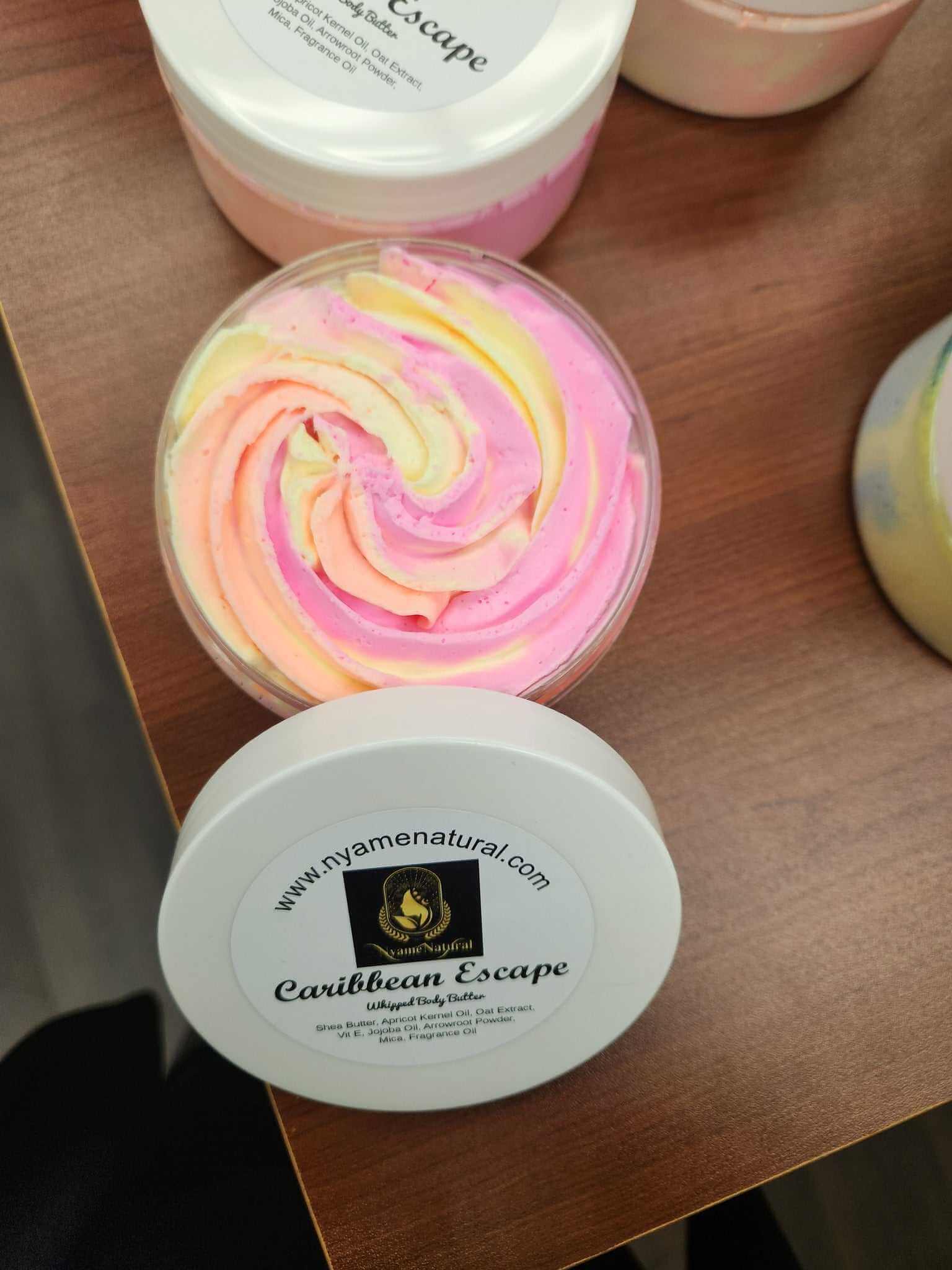 Colorful Caribbean Escape Body Butter in a clear jar on a wooden surface, showcasing its silky texture and rich colors.