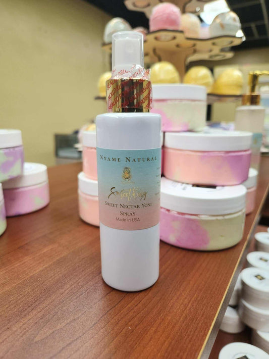 Small bottle of Sweet Yoni Spray on a wooden table surrounded by colorful skincare products.