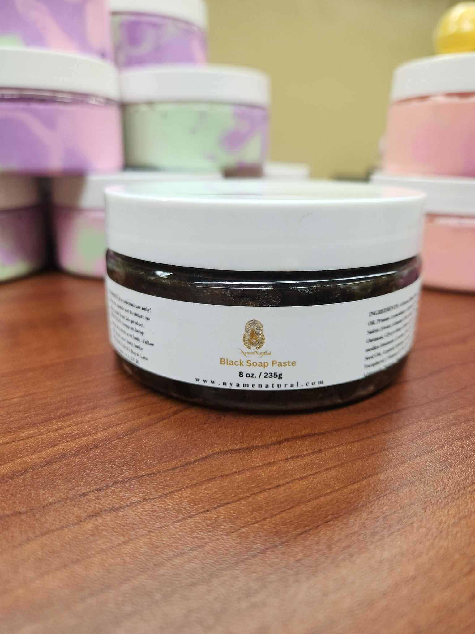 Black soap paste jar on wooden surface, promoting acne reduction and even skin tone.