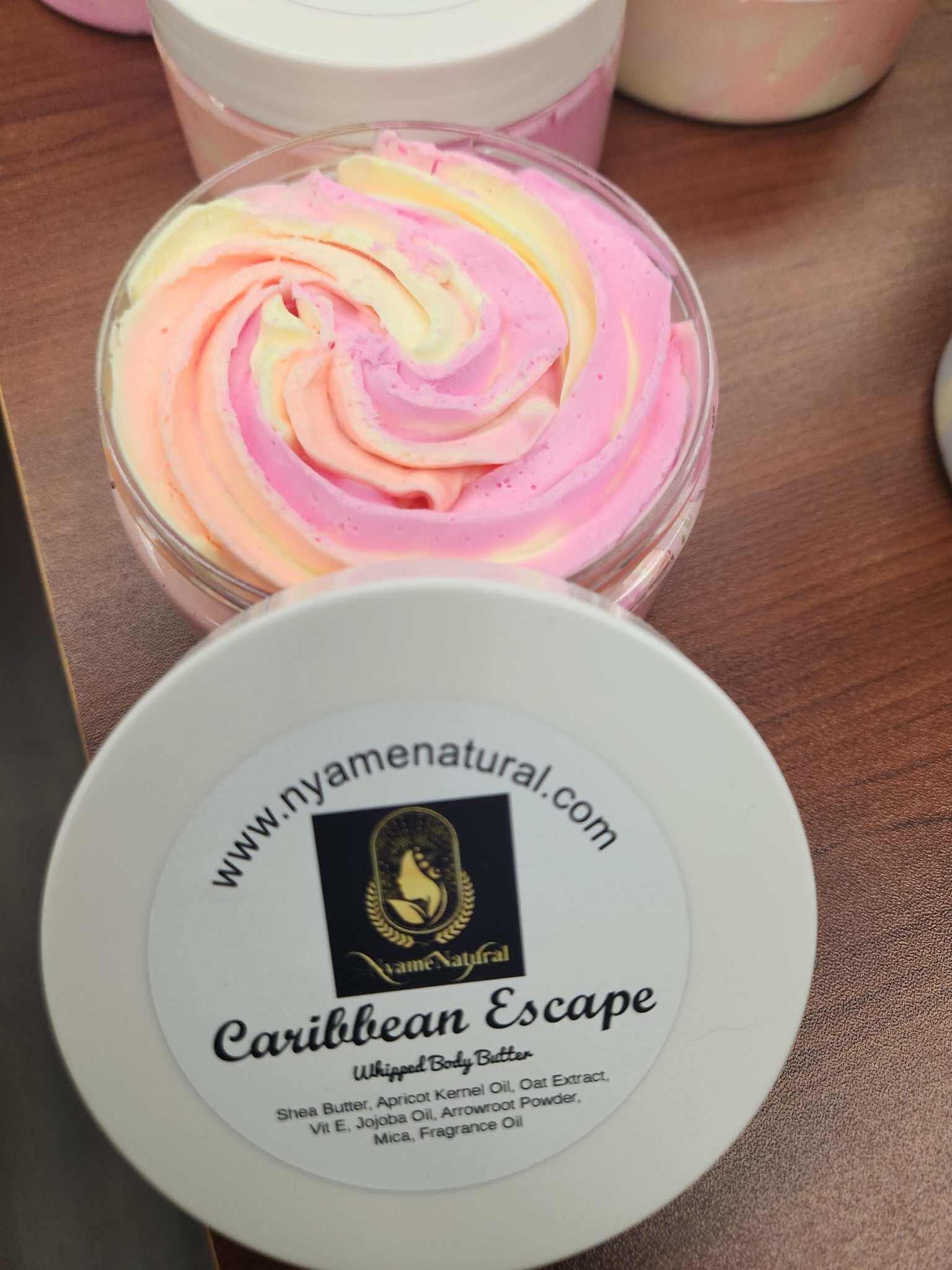 Colorful Caribbean Escape Body Butter with a creamy swirled texture in a clear jar on a wooden surface.