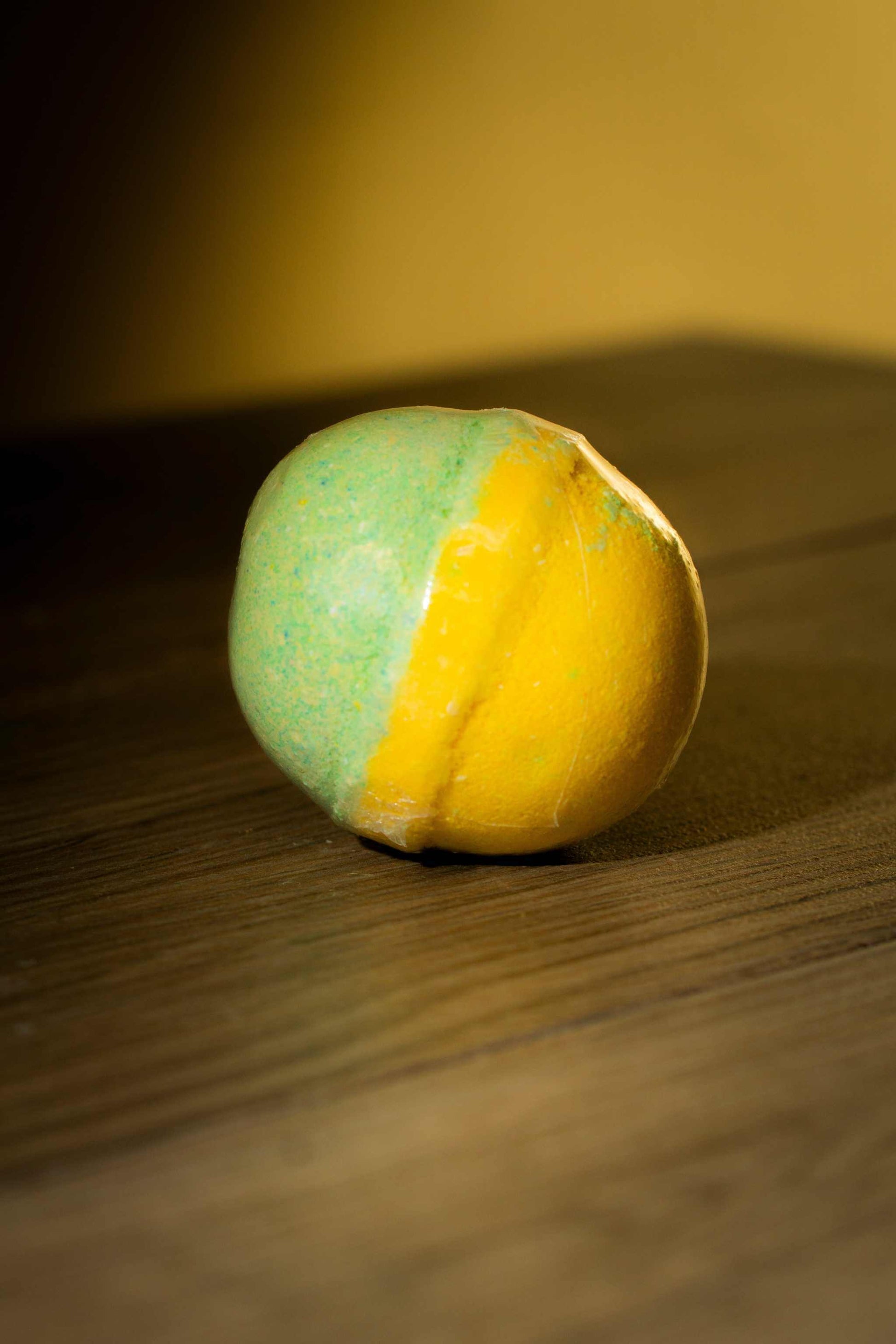 Vibrant green and yellow Luxurious Body Bath Bomb on a wooden surface, ideal for a soothing bath experience.