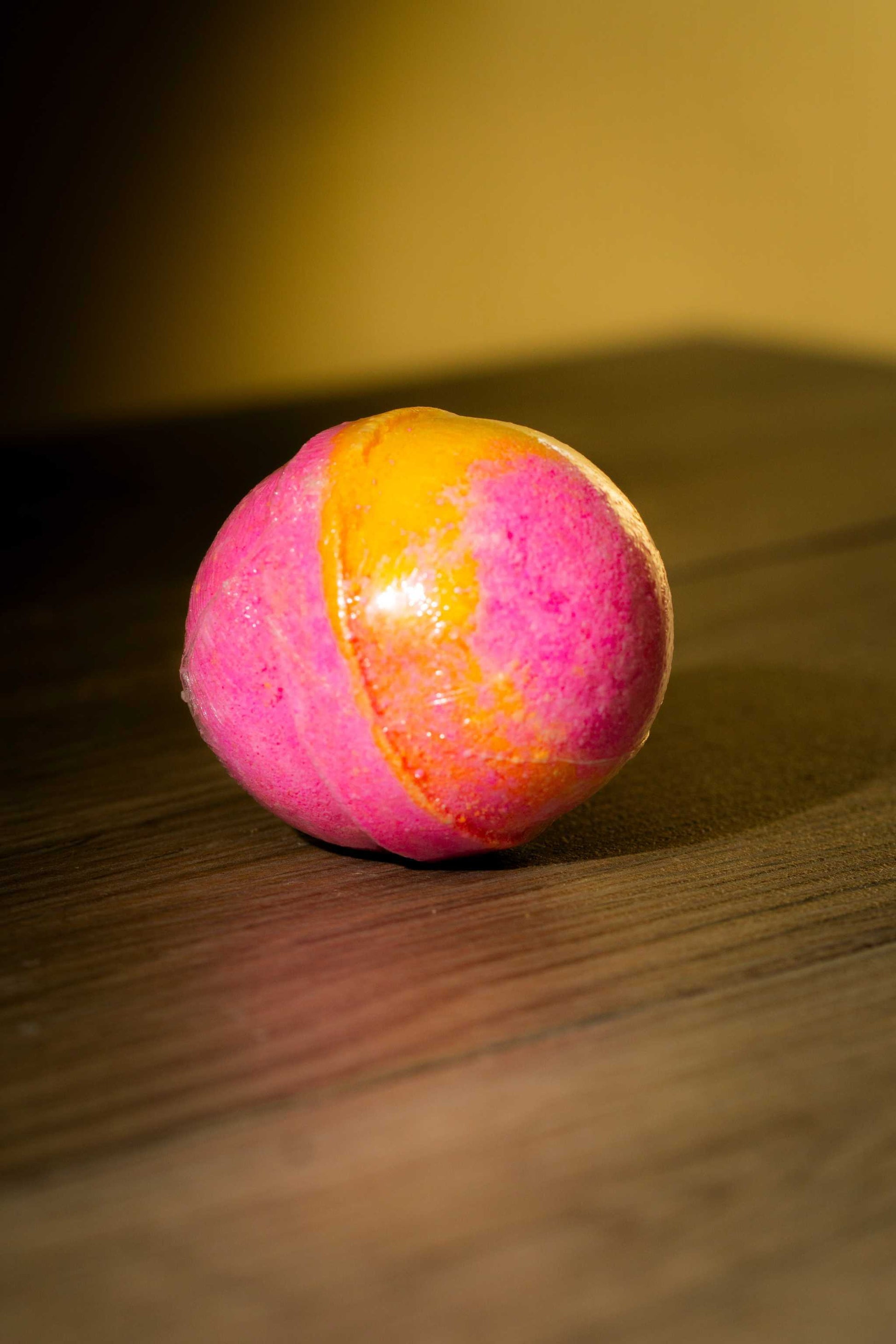 Luxurious body bath bomb in vibrant pink and orange colors resting on a wooden surface.