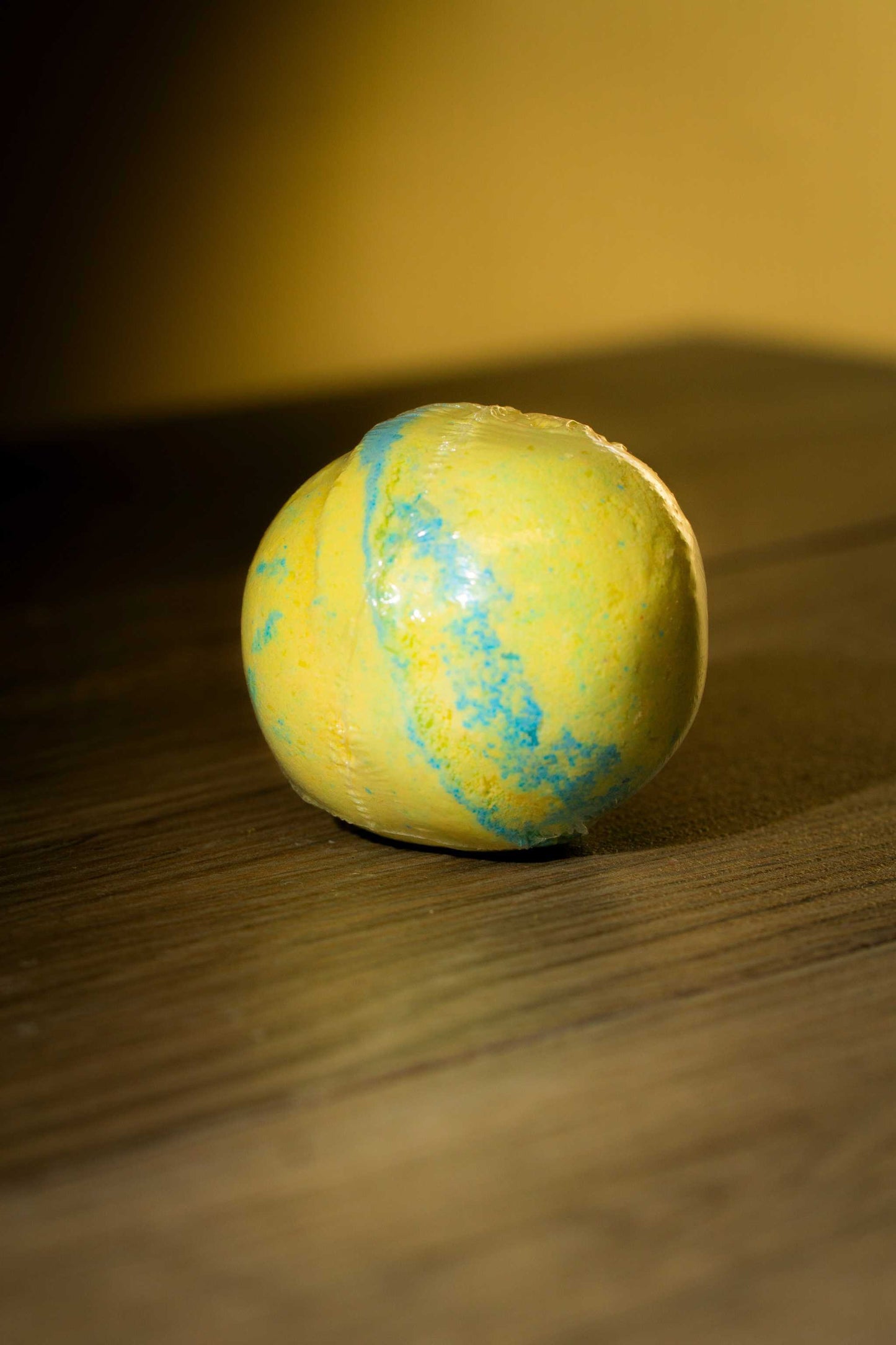 Vibrant yellow and blue Luxurious Body Bath Bomb on wooden surface, perfect for a soothing soak.