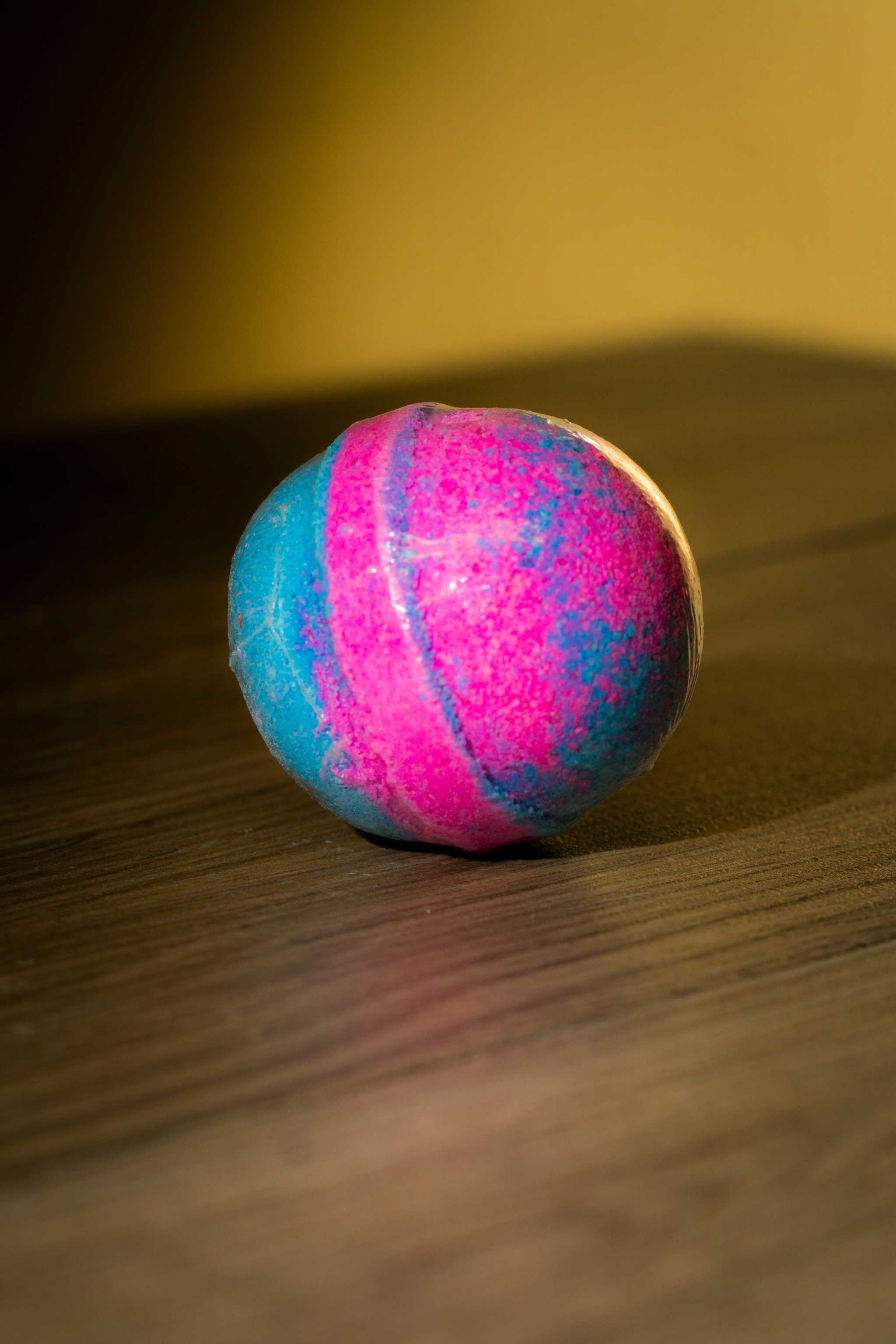Vibrant pink and blue Luxurious Body Bath Bomb resting on a wooden surface.