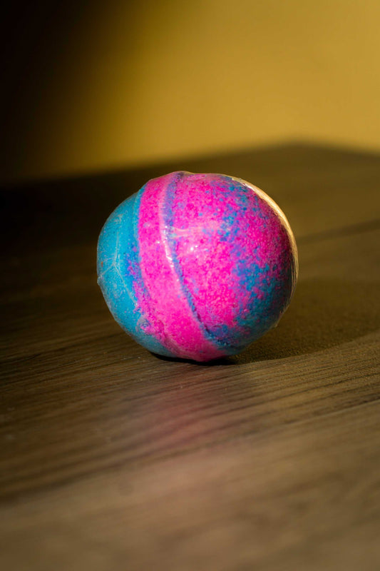 Vibrant pink and blue Luxurious Body Bath Bomb resting on a wooden surface.
