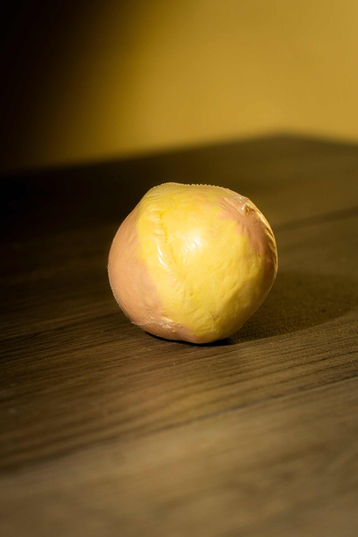Luxurious body bath bomb in vibrant yellow and pink hues on a wooden surface, perfect for a calming soak.
