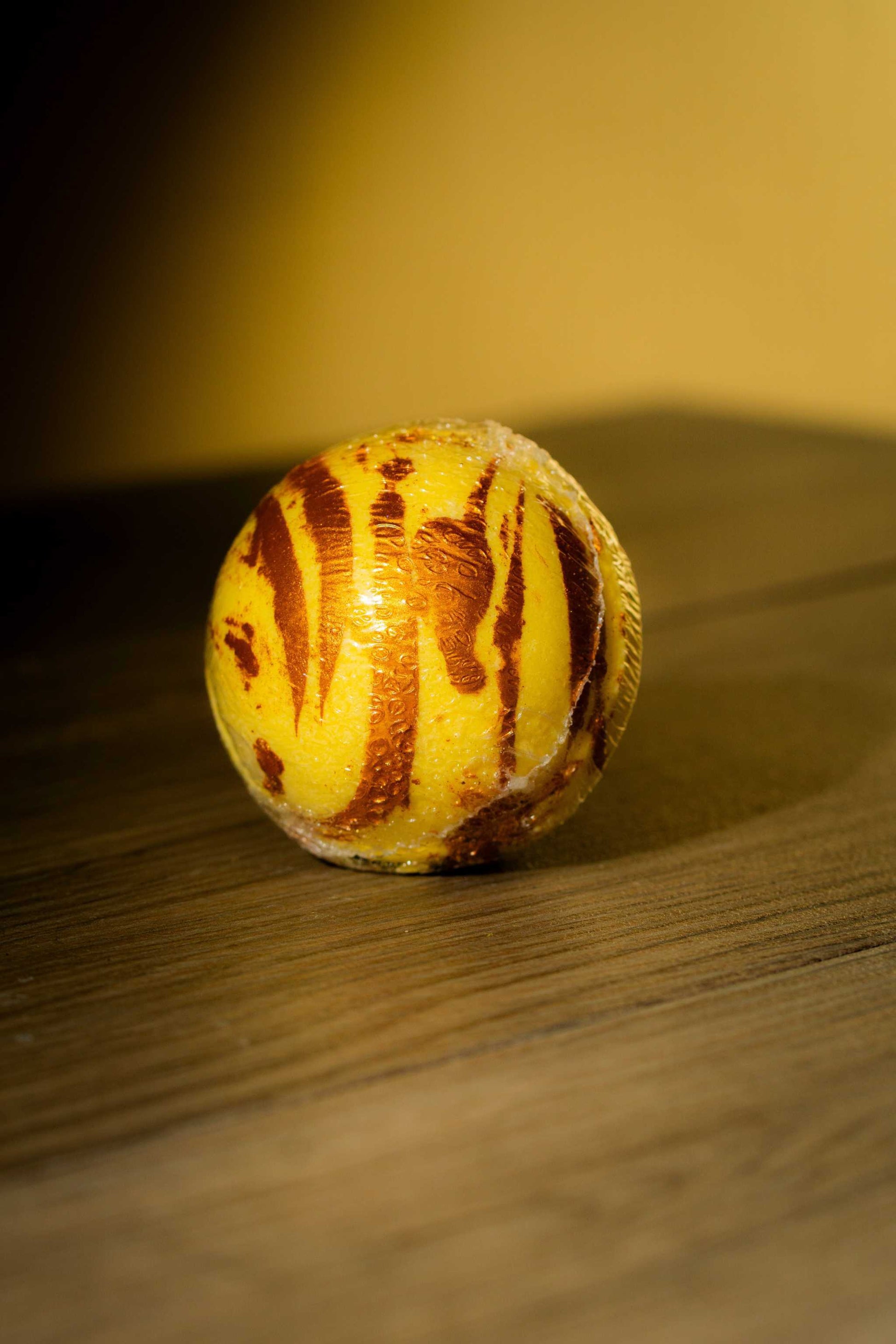 Vibrant yellow and brown striped luxurious body bath bomb on wooden surface.