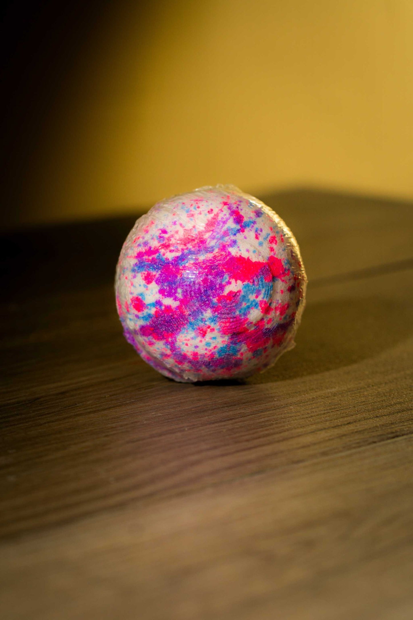 Vibrant Luxurious Body Bath Bomb with a mix of pink, purple, and blue colors on a wooden surface.