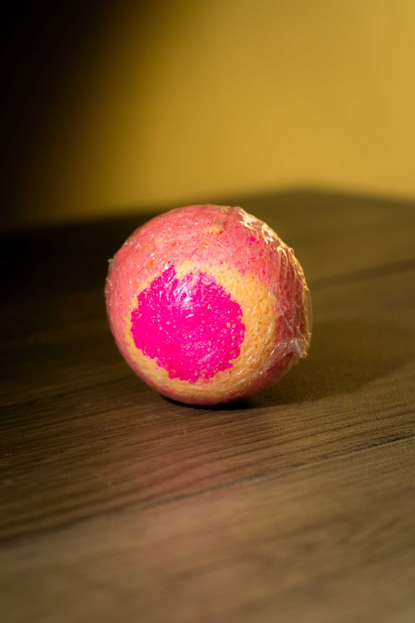 Colorful Luxurious Body Bath Bomb on wooden surface, featuring vibrant pink and yellow hues.