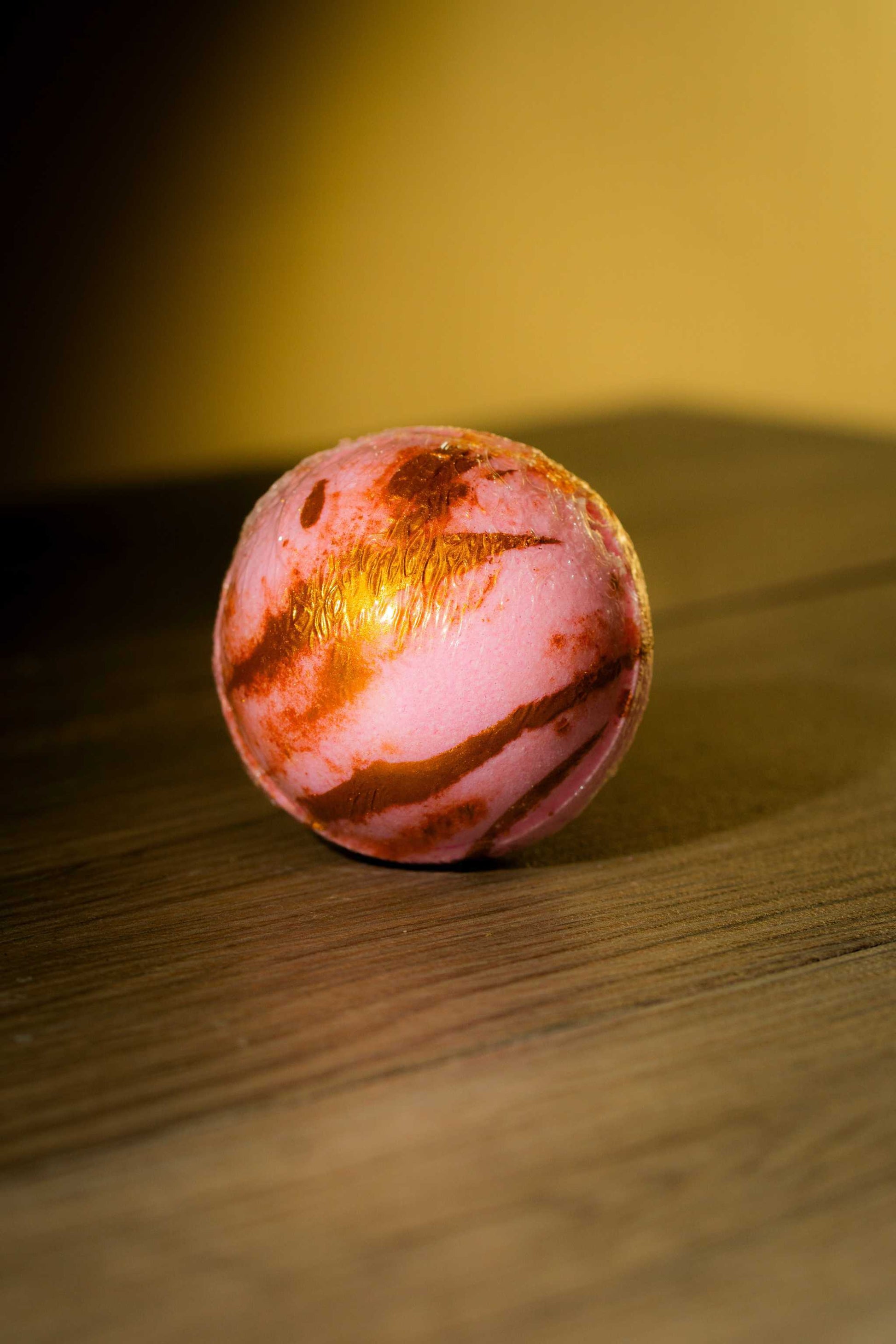 Luxurious Body Bath Bomb in pink and gold hues on a wooden surface.