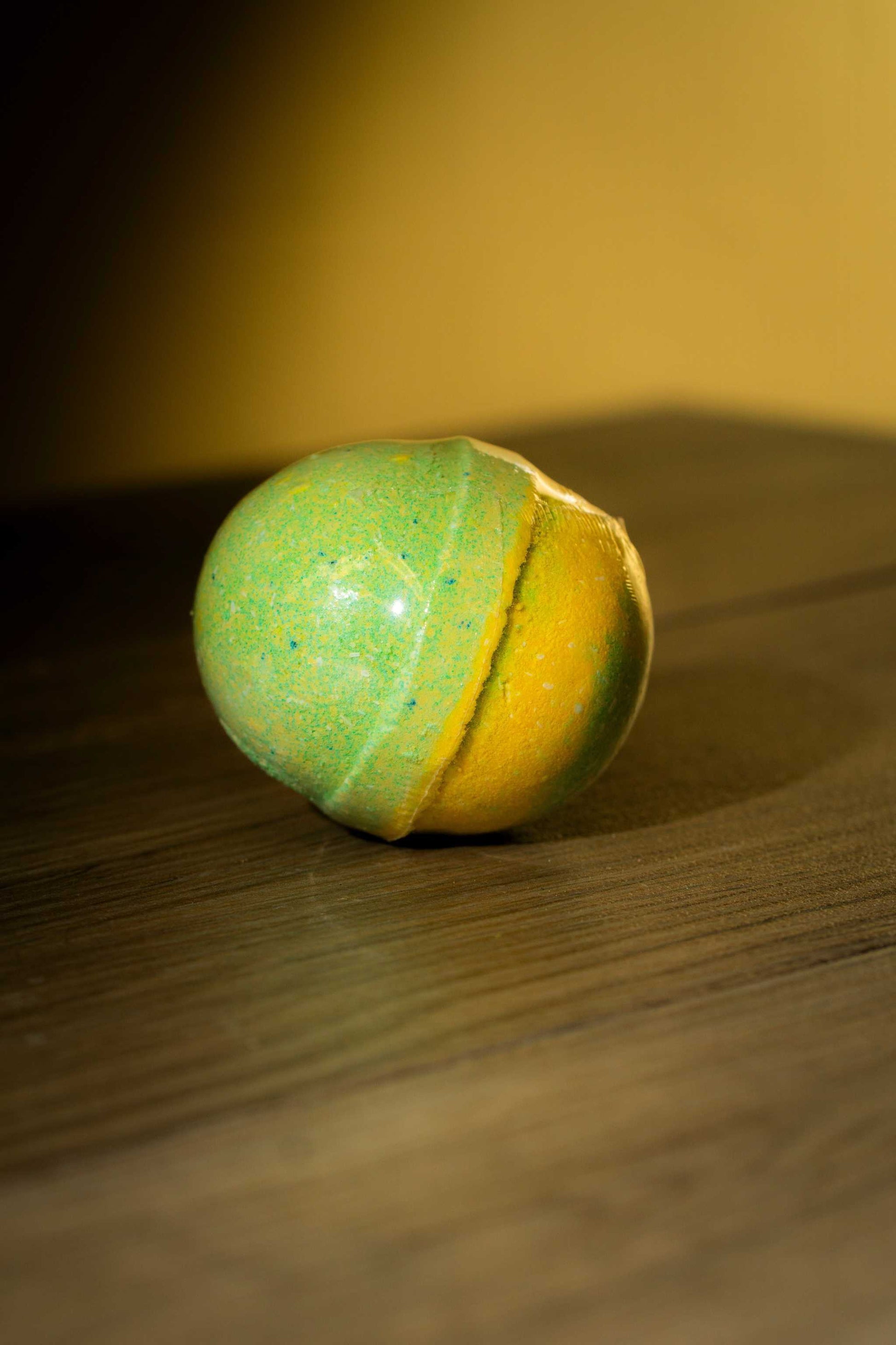 Vibrant green and yellow Luxurious Body Bath Bomb on wooden surface for relaxing self-care.