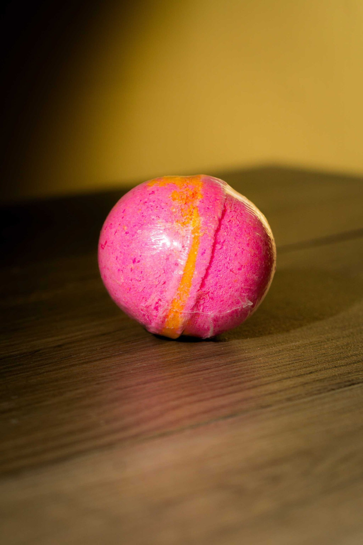 Luxurious pink and orange body bath bomb resting on a wooden surface, perfect for a rejuvenating bath experience.