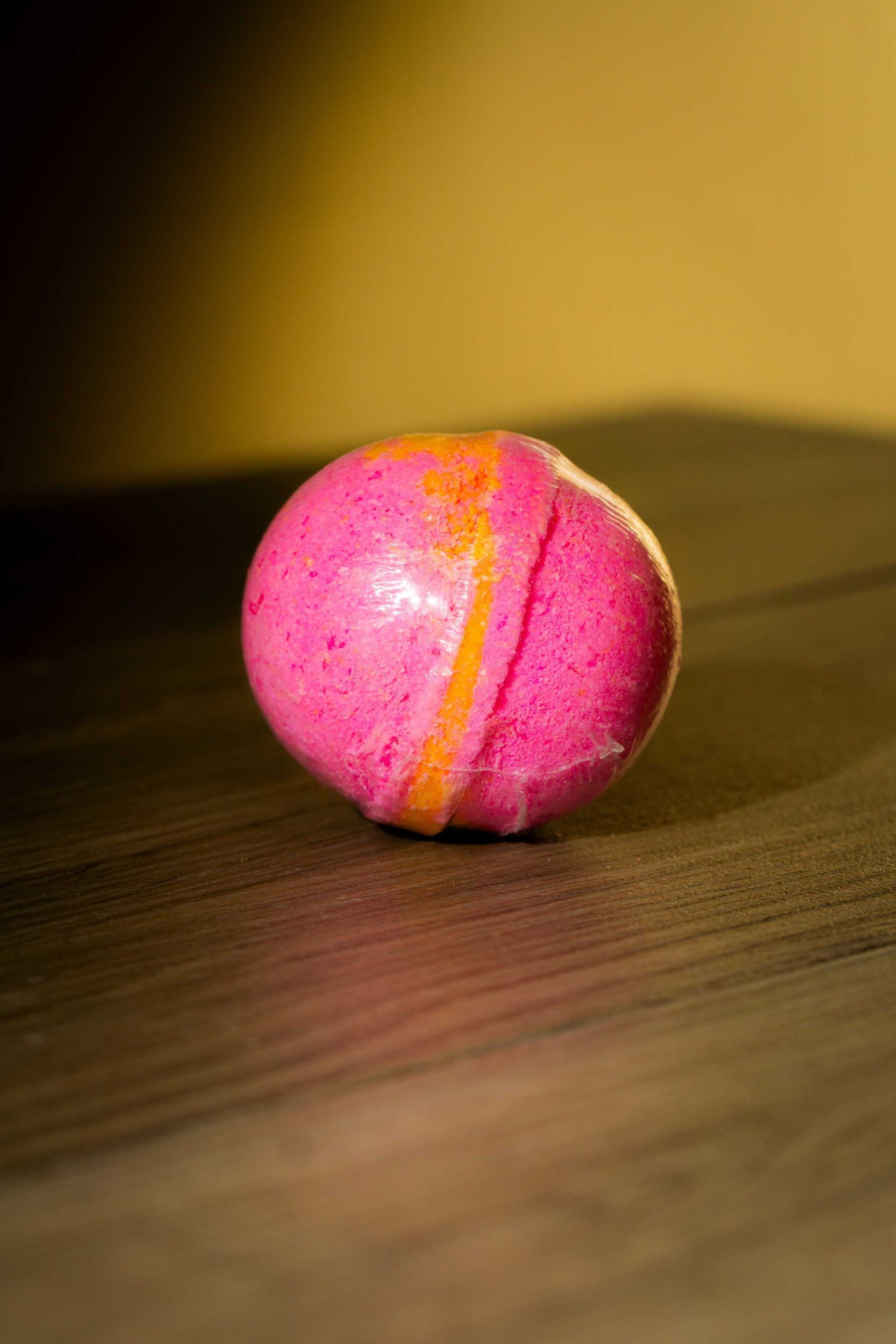 Luxurious pink and orange body bath bomb resting on a wooden surface, perfect for a rejuvenating bath experience.