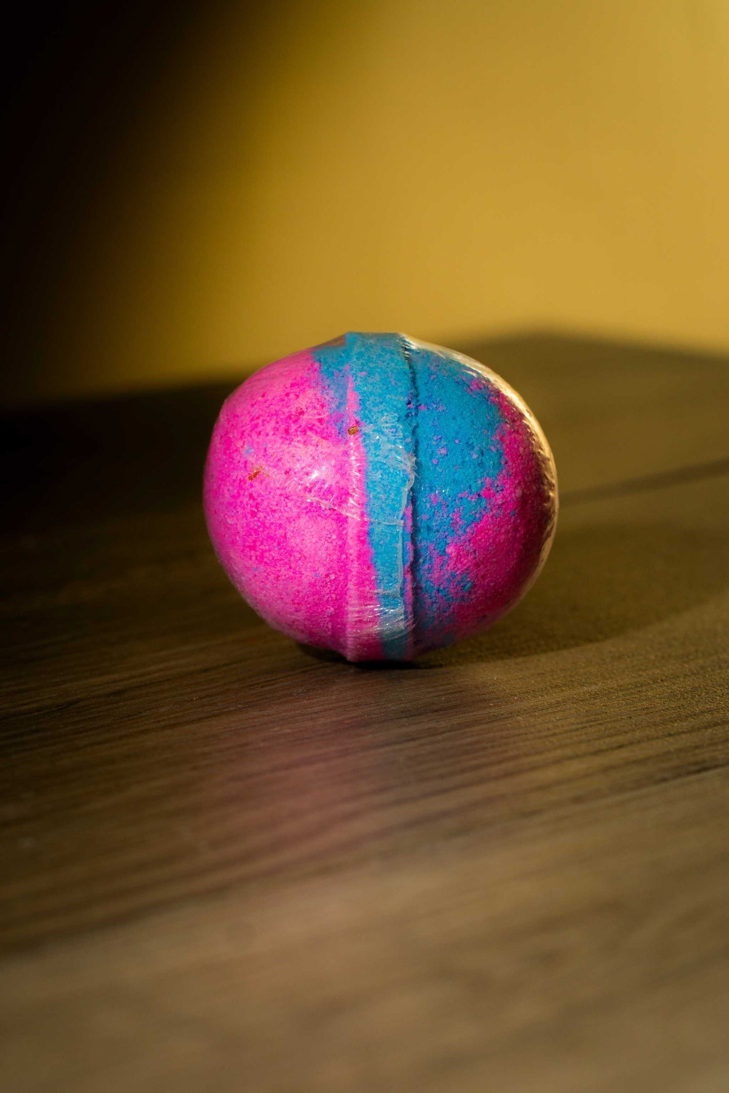 Colorful pink and blue Luxurious Body Bath Bomb resting on a wooden surface, perfect for a soothing soak.