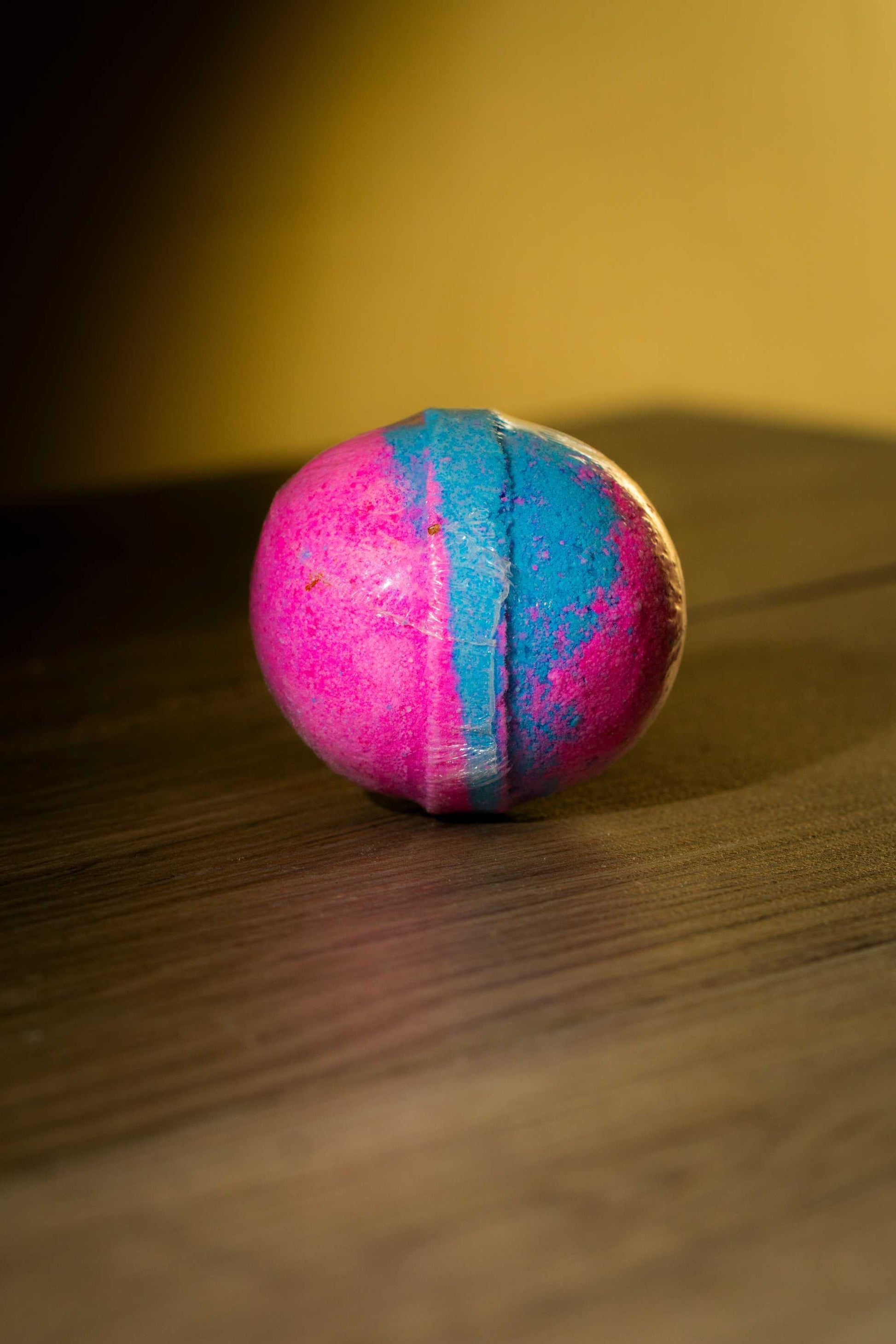 Colorful pink and blue Luxurious Body Bath Bomb resting on a wooden surface, perfect for a soothing soak.