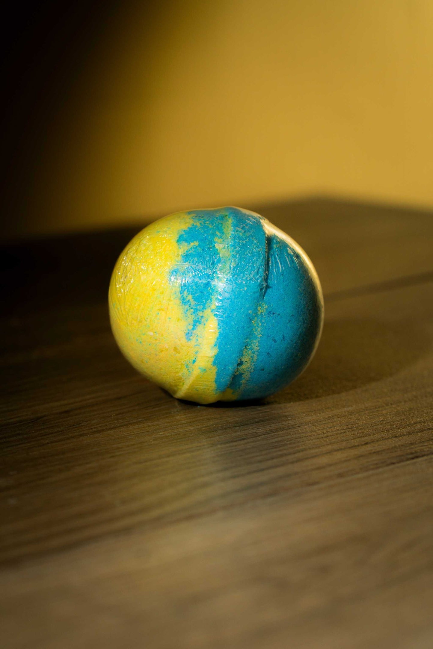 Luxurious body bath bomb in vibrant blue and yellow colors on a wooden surface, perfect for a rejuvenating soak.