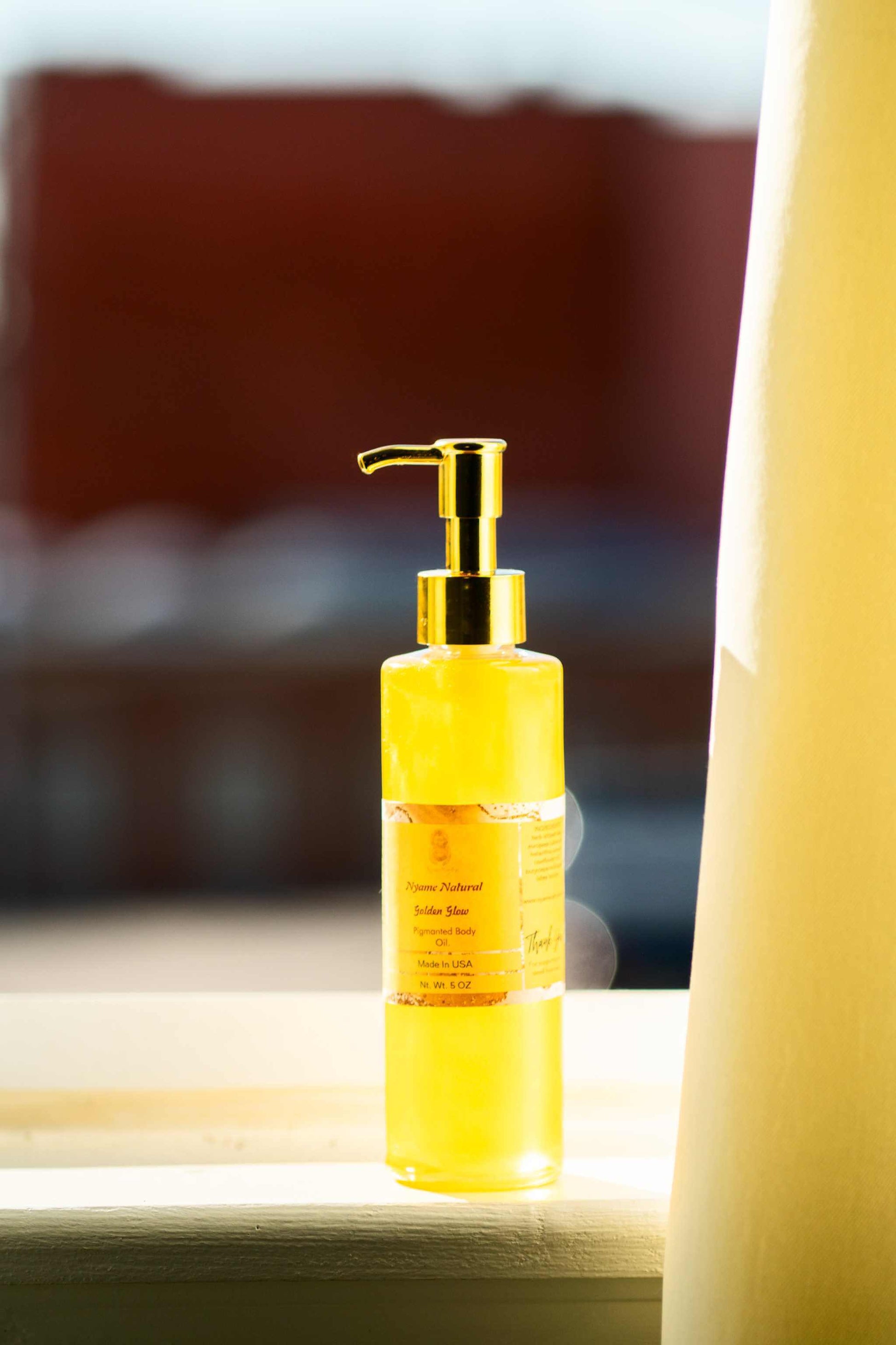 Luxurious 24k Gold Pigmented Pheromone Body Oil in a glass pump bottle capturing sunlight.