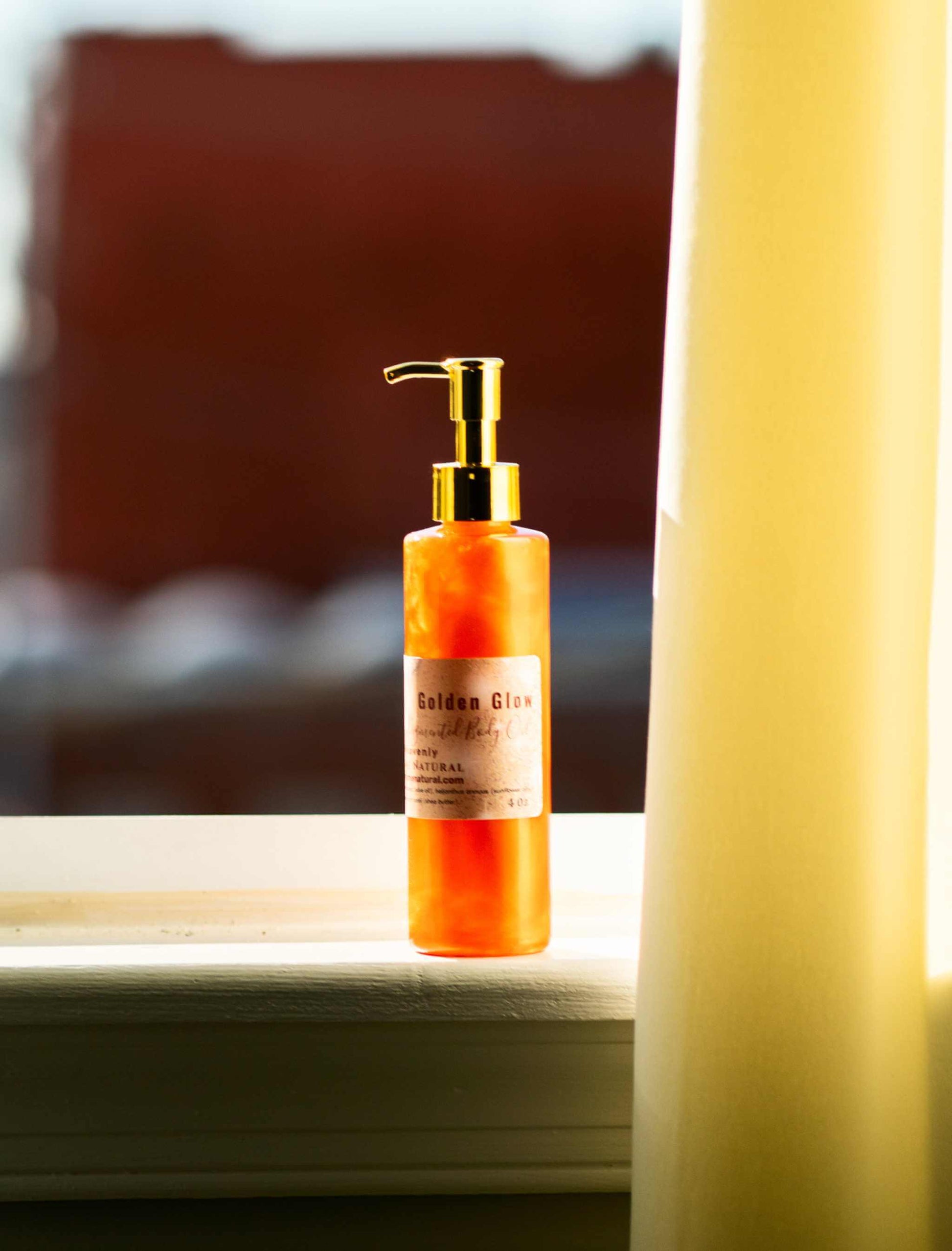 Golden Glow body oil bottle with pump on a windowsill, showcasing its beautiful copper pigmentation.
