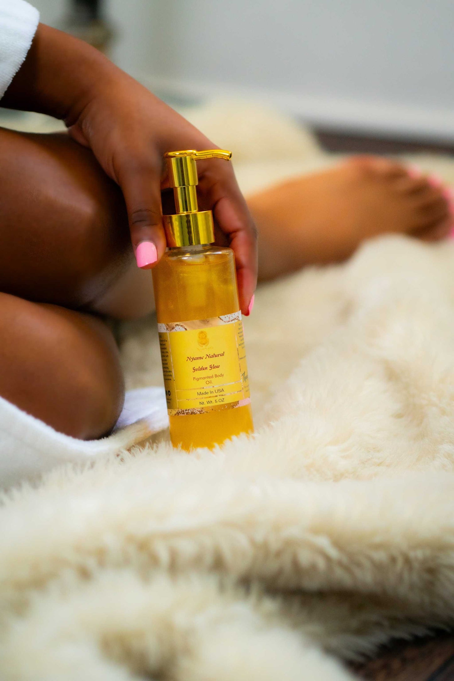 Hand holding a bottle of 24k Gold Pigmented Pheromone Body Oil on a soft rug.