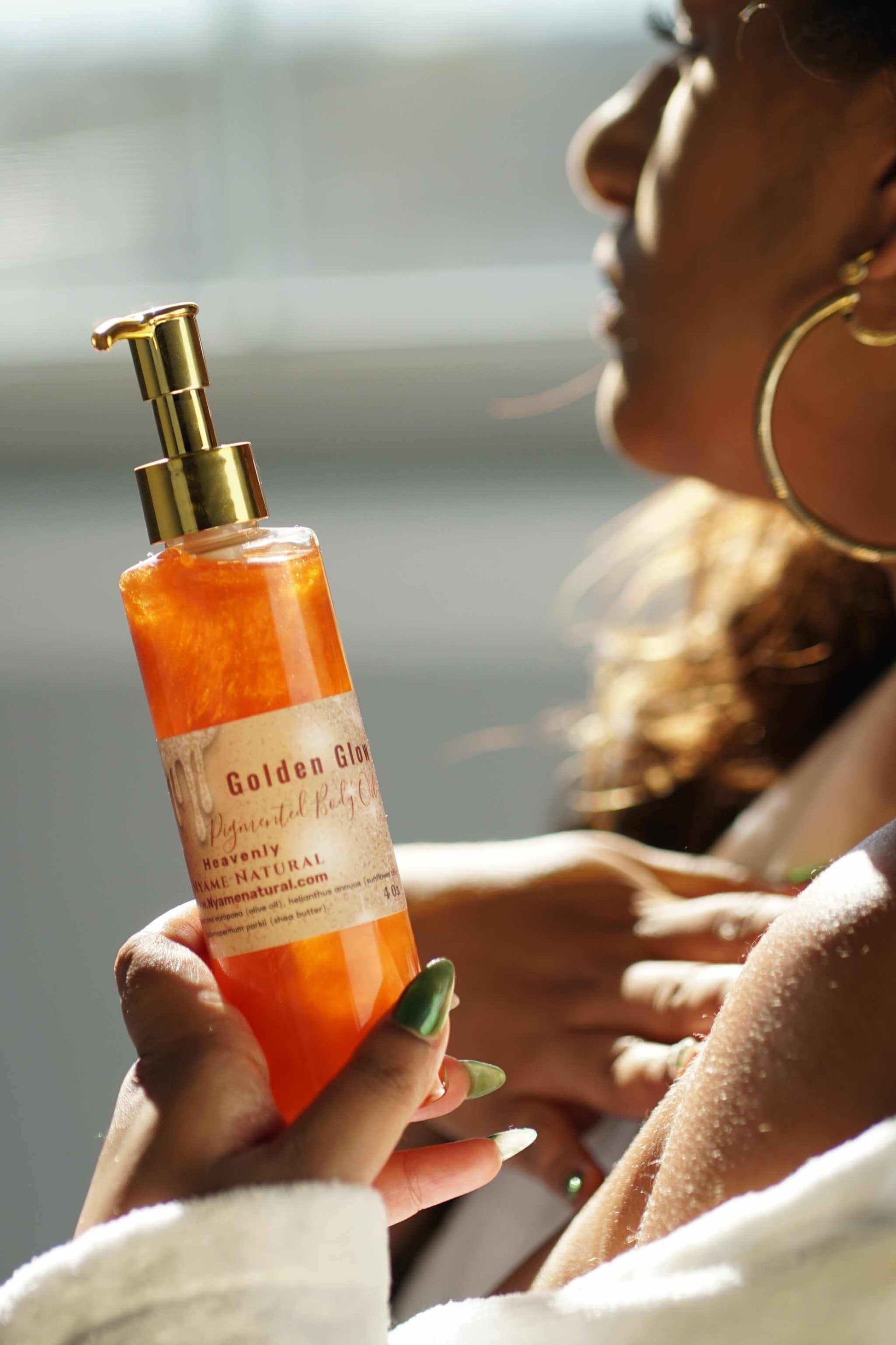 A woman holding a bottle of Golden Glo body oil, showcasing its radiant copper color and luxurious packaging.