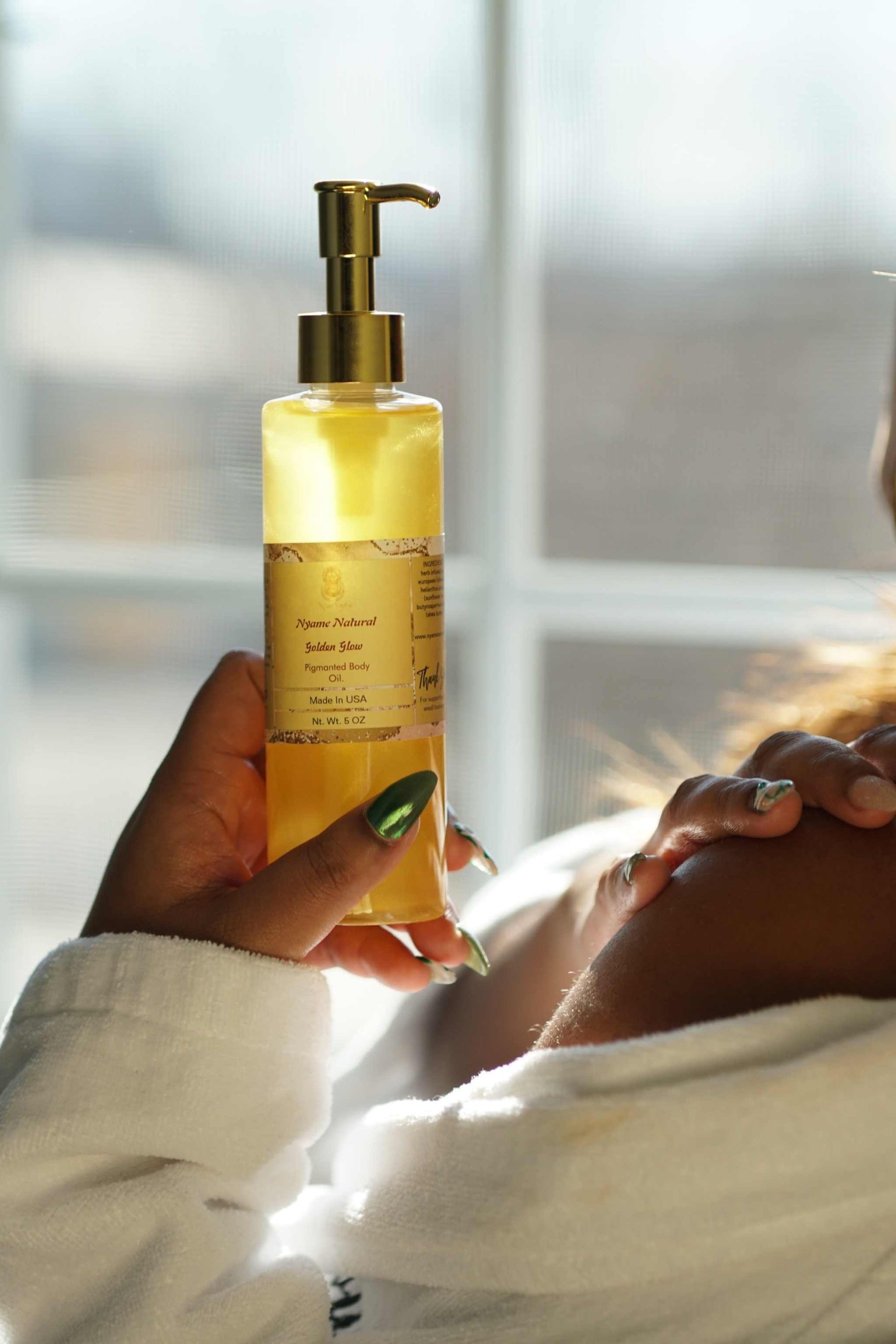 Person holding a bottle of 24k gold pigmented pheromone body oil, showcasing its luxurious texture.