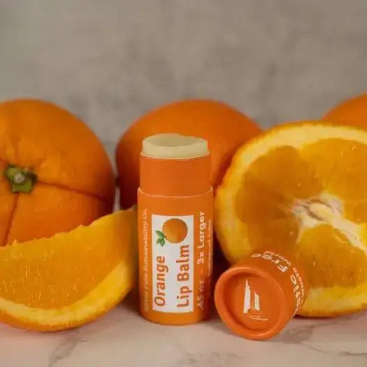 Orange Lip Balm tube surrounded by fresh oranges, highlighting its natural ingredients and vibrant color.